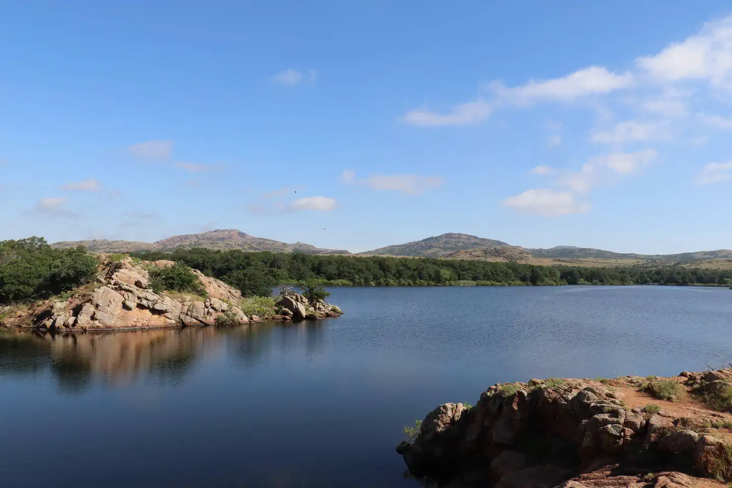 The Wichita Mountains line the horizon beyond the pink granite shore of Quanah Parker Lake.