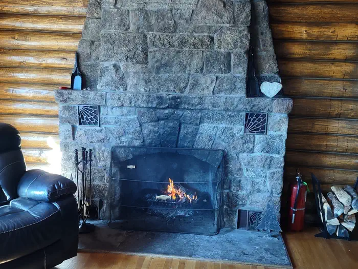 Stone fireplace, chair, logs, fireplace tools (poker, shovel, broom) and fire extinguisher.