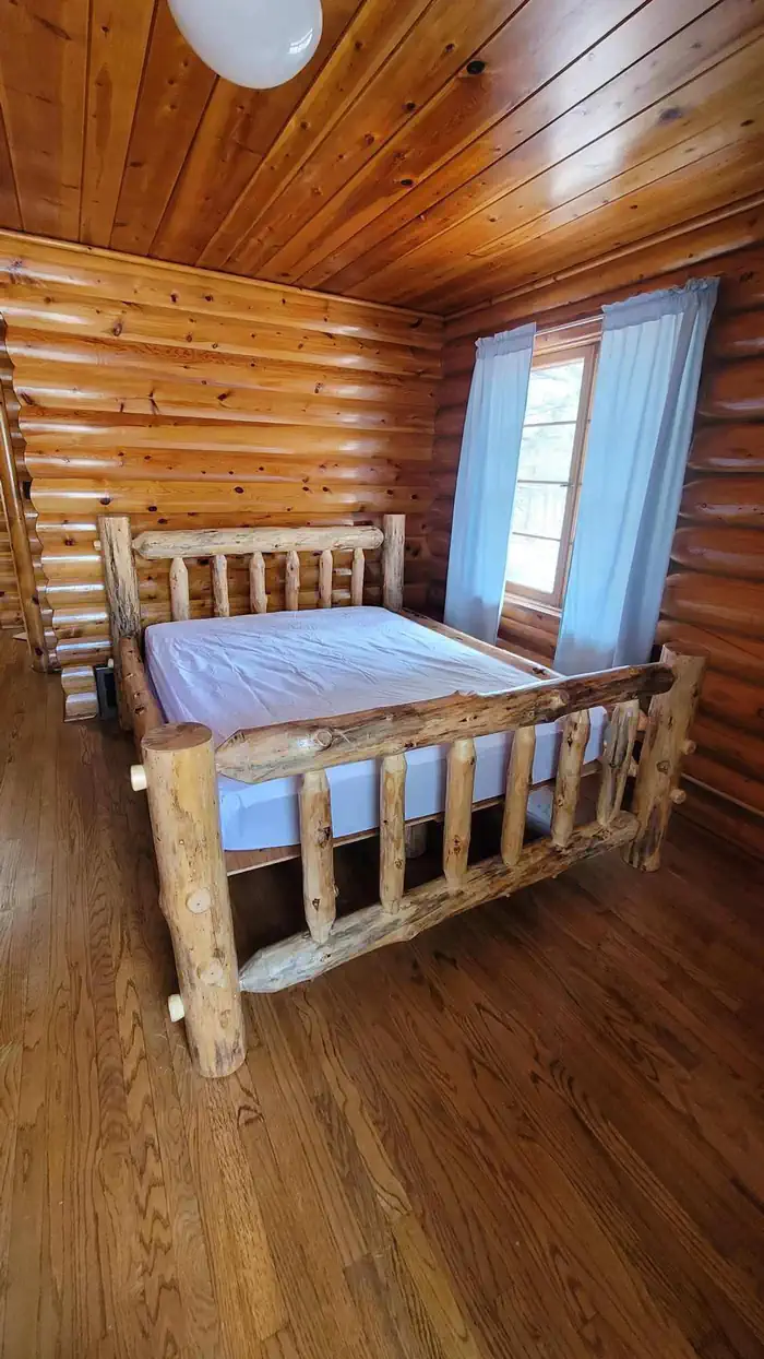 Log bed in log cabin with wood floors and log walls and wood ceiling.
