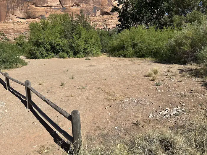 Kings Bottom Group Site has a wide tent space for several tents based on tent size. The surface is flattened gravel and sand and is surrounded by tall vegetation.