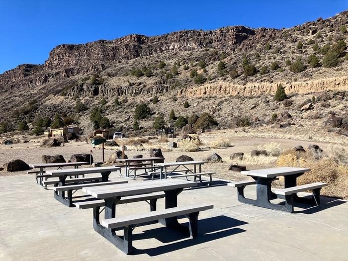 A view of the Taos Junction group site area with picnic tables, concrete pad, fire pan, and trash receptacles.