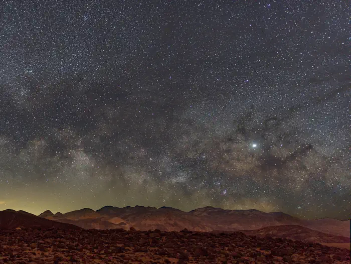 Mountains in foreground, clear night sky filled with stars in background.