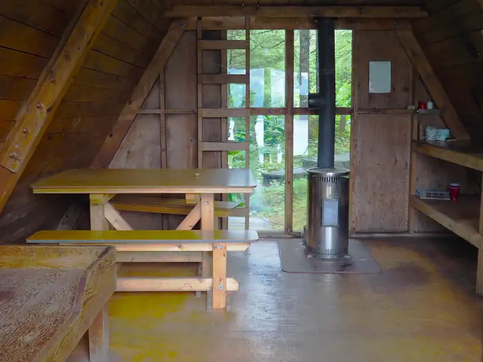 Berg Bay Cabin interior with window, wooden ladder, table and oil stove.