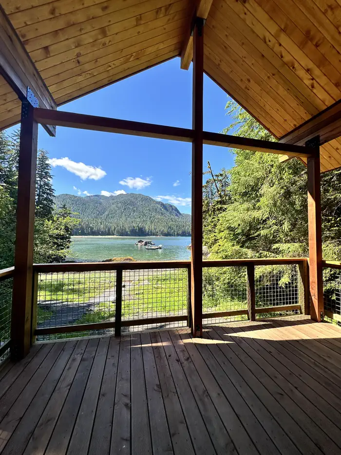 Deck with view of boat and floathouse in bay and mountains in background.