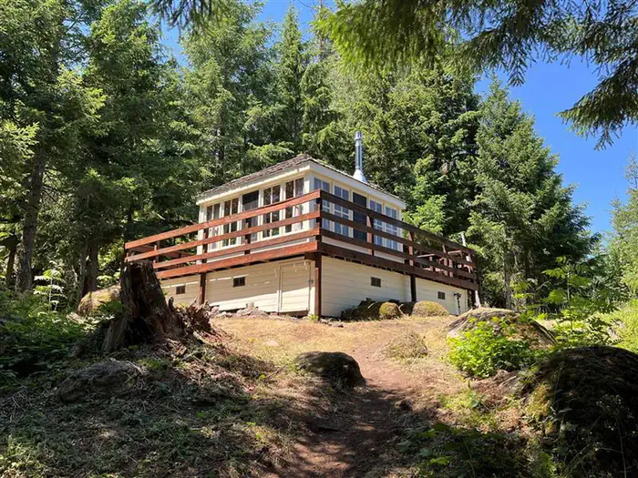 Trail leading to white cabin with wrap around porch, surrounded by fir trees