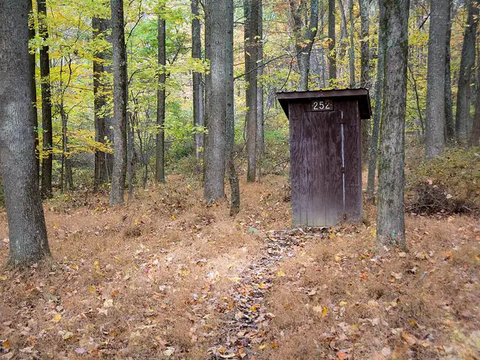 Small enclosed wooden pit toilet building. Surrounded by trees in late fall.