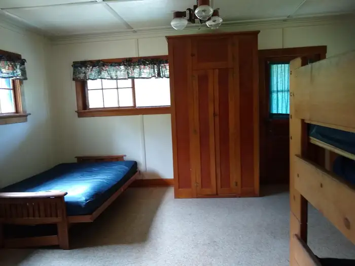 A tall cabinet next to a futon bed, with a bunkbed frame in the foreground.