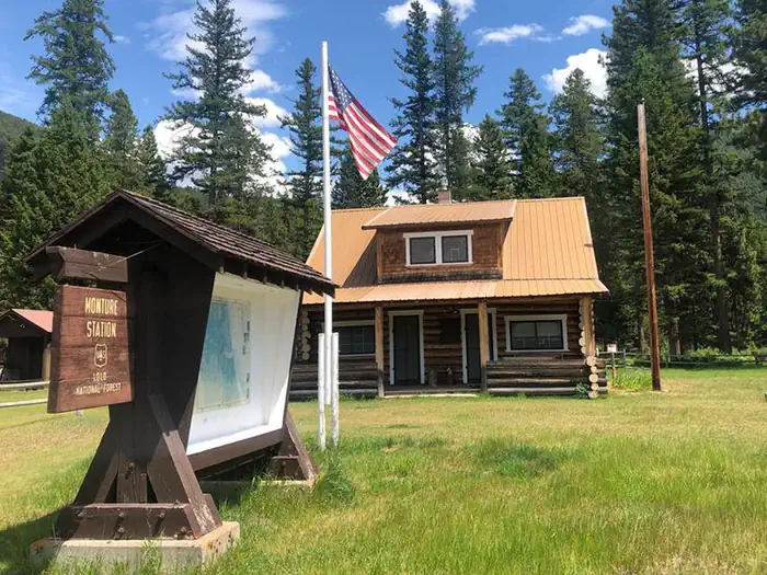 Monture Guard Station Rental Cabin in the Summertime. An American Flag Waves in the Front Yard.