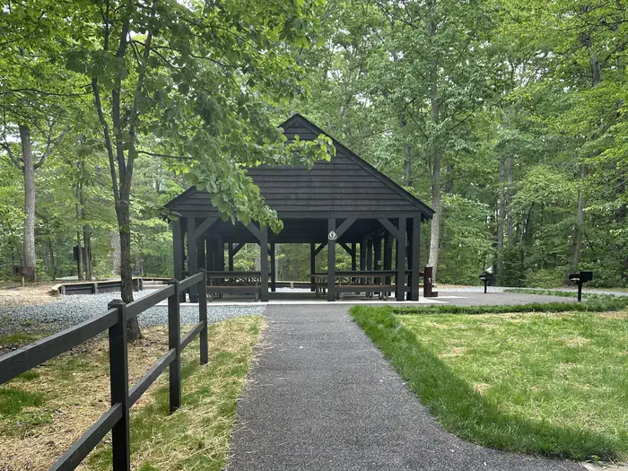 Paved walkway leading to a wooden roofed and paved picnic pavilion shaded by trees