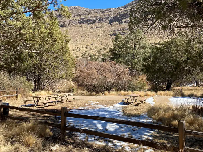 Dog Canyon Group Campsite with two tent pads delineated with landscape timbers and filled with fine crushed gravel. Three picnic tables are located in an open grassy area for groups to gather.
