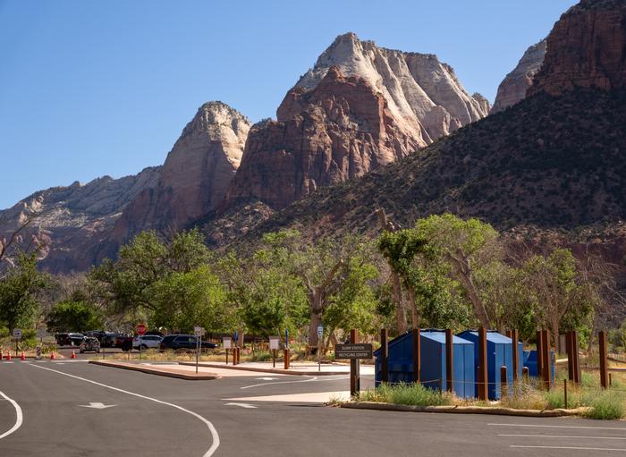 Recreational vehicle water fill and dump station with recycling and trash bins at the entrance to South Campground in Zion National Park, with dramatic sandstone cliffs rising in the background.