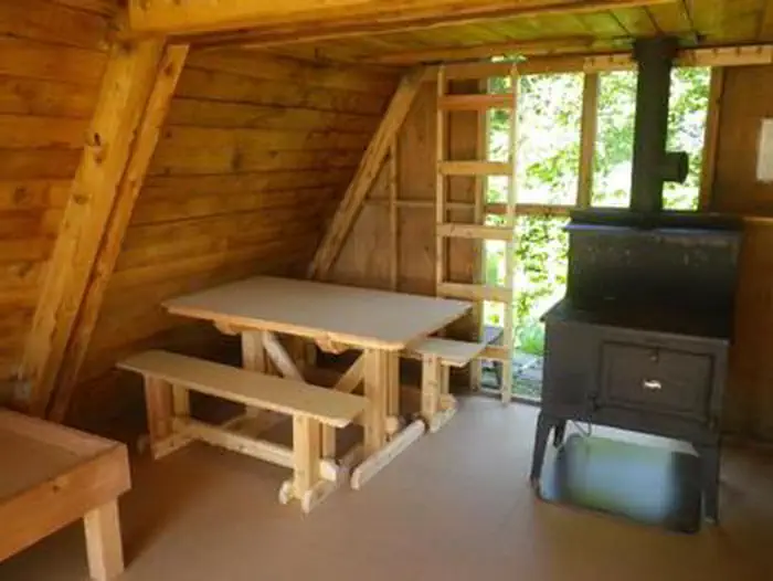 Twin Lakes Cabin (AK) interior showing wood table and stove with vertical ladder to loft