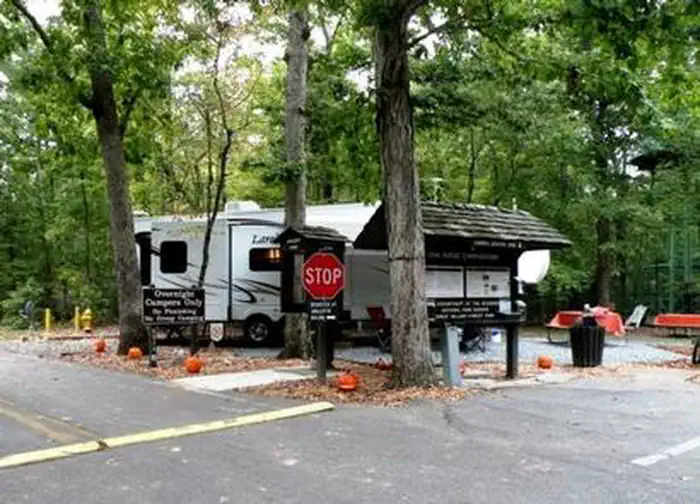 Large white RV sits behind a stop sign and information sign along a roadway in the forest