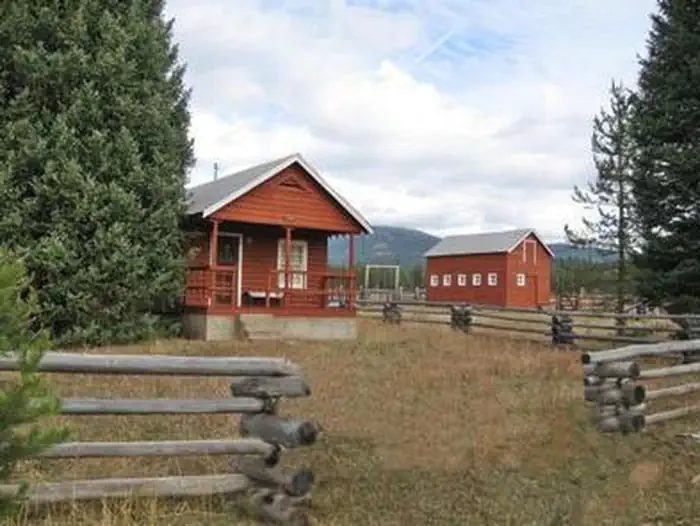 Paddy Flat Guard Station Cabin East at a medium distance with rustic fence and trees. Barn in the background.