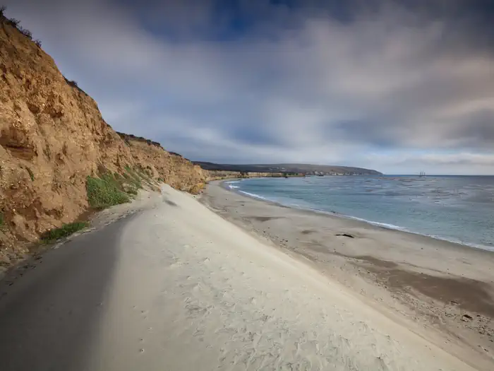 White sand dune next to a steep coastal bluff with ocean